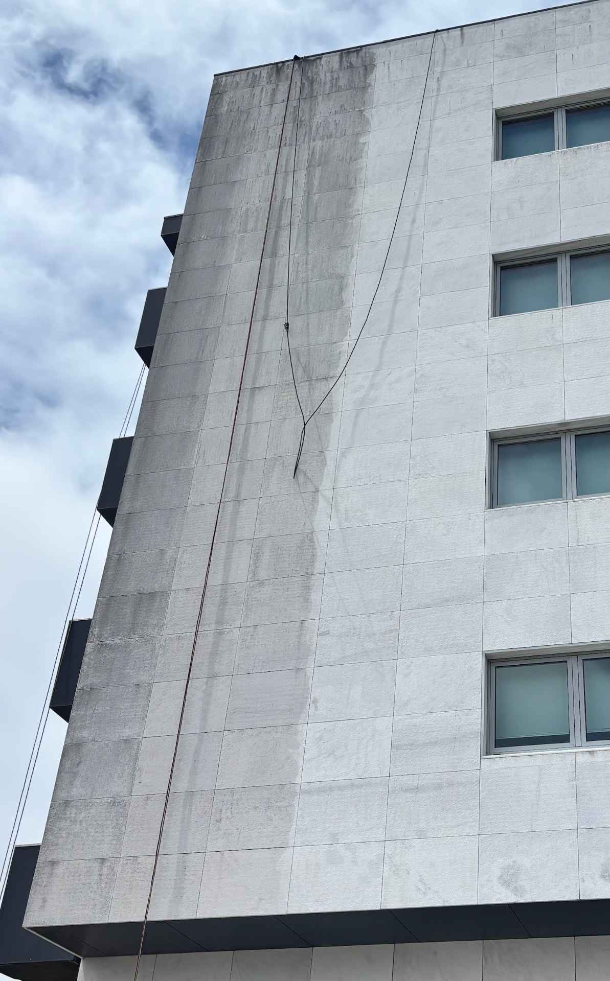 Fachada de edifício com sujidade acumulada e cordas de acesso